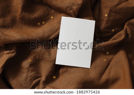 Blank vertical greeting card mock-up scene. Rusty linen table cloth background with golden confetti stars. Happy New Year invitation. Celebration, party concept. Flat lay, top view.
