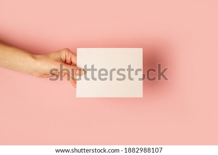 Female hand holding a card on a pastel pink background. Flat lay, top view