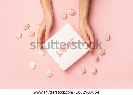 Female hands are holding a gift with the inscription Love on a pastel pink background with meringues. Valentine's Day concept. Banner. Flat lay, top view