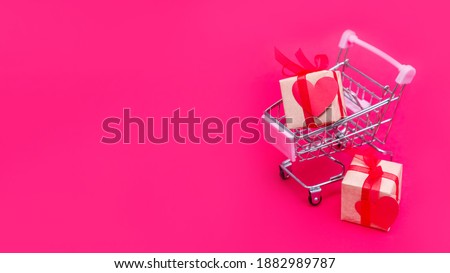 Small grocery cart with gift boxes on red-pink background. Give gifts with love on Valentine's Day, Christmas and birthday. Shopping online. Holiday sales and discounts. Retail and wholesale purchase