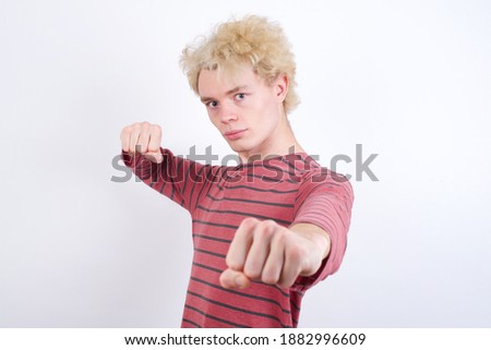 Young handsome Caucasian blond man standing against white background Punching fist to fight, aggressive and angry attack, threat and violence