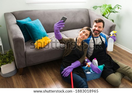 Good looking Hispanic couple wearing gloves and an apron taking a selfie while cleaning and doing house work at home