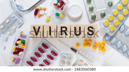 The word VIRUS on wooden blocks on the table. Medical concept with pills, vitamins, stethoscope and syringe in the background.
