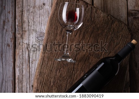 Macro shot of glass with remains of red wine and dark elegant bottle on wooden board on rustic background. Advertising and promotion concept. Mock up. Flat lay. View from above. Space for text.