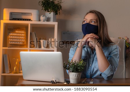 Young woman siting in the office in protective mask and dreams. Concept of coronavirus pandemic in the world.