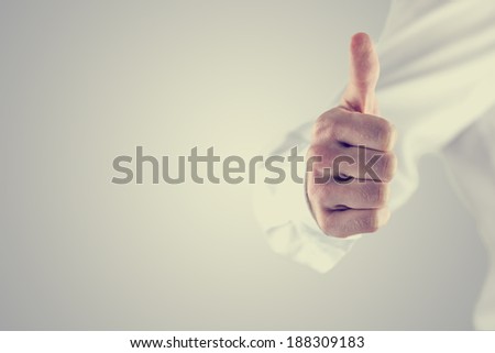 Retro vintage or instagram style image of a man giving a thumbs up gesture of approval and success on a grey background with copyspace.