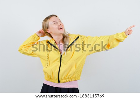  young lady in t-shirt, jacket pointing aside and looking happy , front view. 