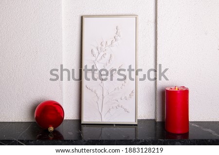 Botanical bas-relief wildflowers for wall art and red christmas ball and candle on marble shelf. 3D Flower plaster decor. Christmas decoration. Stylish and modern interior of room.