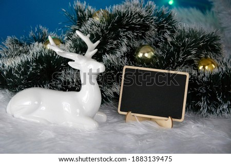 Christmas background, a deer lies near a green spruce branch. Chalk board. Christmas balls decorate the Christmas tree.