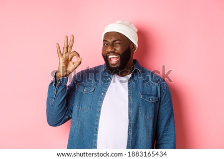 Happy smiling african american man showing okay sign, approve and praise good offer, standing over pink background
