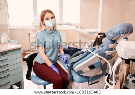 Young woman dentist looking to the camera, sitting beside patient with inhalation sedation at dental office. Concept of sedation dentistry and dental care. Royalty-Free Stock Photo #1883165485