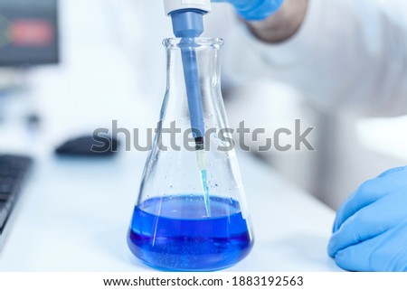 Scientist mesuaring genetic material with micro pipette in laboratory. Senior professional chemist using pippete with blue solution for microbiology tests.