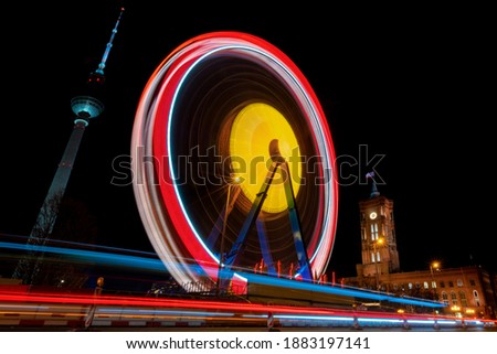 Ferris Wheel with colorful illumination, magical circular light traces at Night with Long Time Exposure in Berlin at christmas with TV tower and townhall “Rotes Rathaus“ in the Background