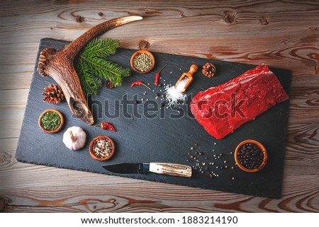 Raw Steak meat from deer on the bridlic  chopping board  with ingredients as a sea salt, garlic, pepper , chilli and other. On the table is deer antler as a decoration.