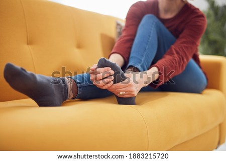Woman with feet intense pain sitting on a couch at home.