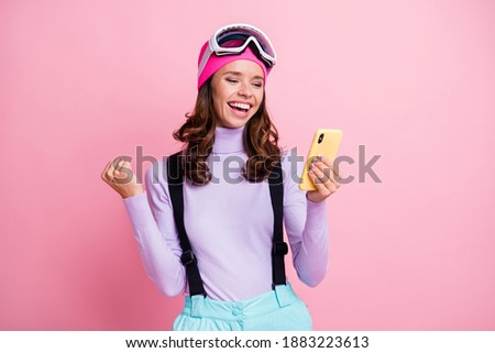 Photo of lucky wavy young woman border wear sweater glasses looking modern device rising fist isolated pink color background