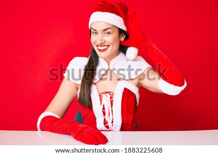 Young caucasian woman wearing santa claus costume smiling with hand over ear listening an hearing to rumor or gossip. deafness concept. 