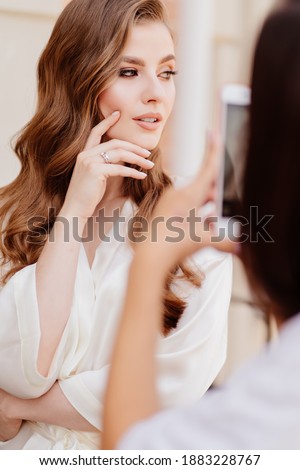 A beautiful young woman in white clothes is photographed on phone, takes photos for social networks. the morning of the bride. Professional makeup.