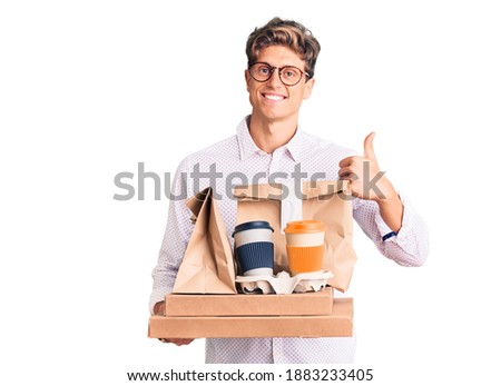 Young handsome man wearing business clothes holding delivery food smiling happy and positive, thumb up doing excellent and approval sign 