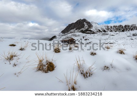 House in a snow-covered field against the background of mountains covered with fog and clouds
