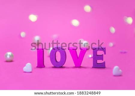 Different colors letters in LOVE word with bokeh, pearls and white heart on pink background. Valentines Day, love and romance, greeting card.