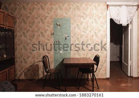Example of Old Soviet Russian poor interior in Khruschev House. Aged  sideboard, table, chairs, sofa. Shabby floor. Tattered wallpaper on the wall. Paper butterflies as decor. Apartment of pensioners. Royalty-Free Stock Photo #1883270161