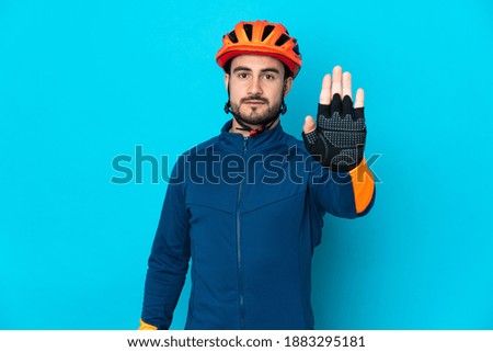 Young cyclist man isolated on blue background making stop gesture