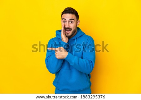 Young caucasian handsome man isolated on yellow background pointing to the side to present a product and whispering something Royalty-Free Stock Photo #1883295376