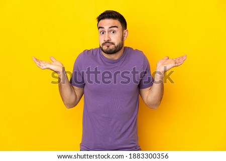 Young caucasian handsome man isolated on yellow background having doubts while raising hands