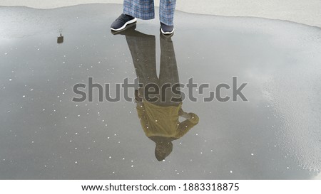 The underwater reflection of a woman in casual style is standing in a cloudy sky
