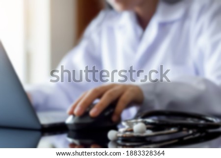 Blurred image of female doctor hand using wireless mouse and work on laptop computer with medical stethoscope on the table at office. Telehealth, telemedicine, emr, ehr or online medical concept.