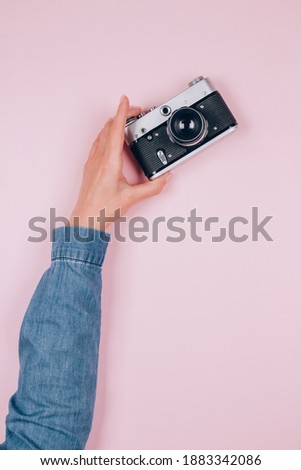 Female hand holding old retro photo camera on pink background with copy space for text. Trendy vintage photography, online photography school concept. Selective focus, vertical composition