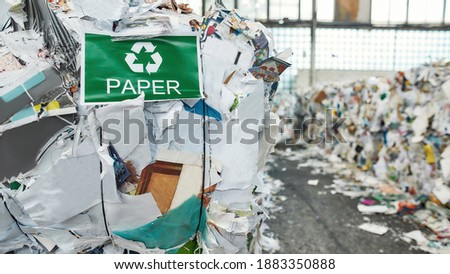 Recycling sign and green arrows on banner hanging on waste paper pile inside rubbish station, widescreen. Garbage sorting and recycling concept