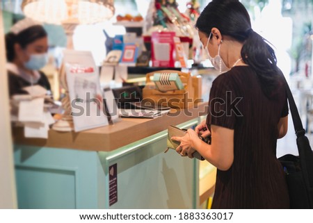 Woman with protective mask paying bill at cashier counter in restaurant
