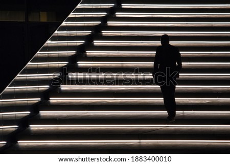 Silhouette of a man walking down steps with lights and reflections Royalty-Free Stock Photo #1883400010