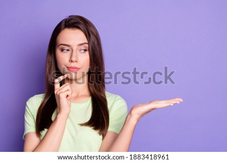 Photo portrait of curious girl touching chin with finger looking at copyspace keeping on palm isolated on bright purple color background