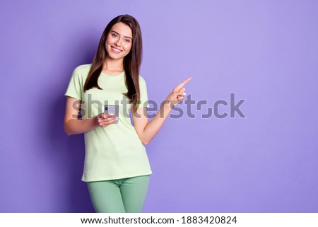 Photo portrait of young brunette using smartphone showing with finger at blank space smiling isolated on vibrant violet color background