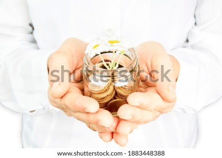 Hand with coins and small flower in a glass jar. Money growth, savings and investment concept.
