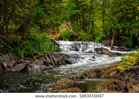 Cordova falls Conservation Area in Havelock Ontario Canada in Autumn featuring Crow River, dark limestone rocks, luscious green forest showing fall colors on a overcast day