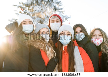 A group photo of friends in winter clothes and special masks on the street. Walking during a pandemic.