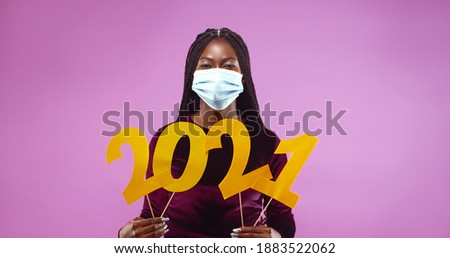 Portrait of young African American woman protective mask holding in hands number 2021 isolated over pink background. New year holiday concept Royalty-Free Stock Photo #1883522062