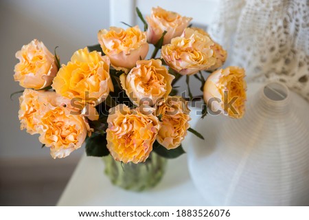 The bouquet of orange roses is in a vase of old green glass on the windowsill from artificial stone.