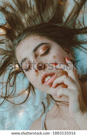 A girl with closed eyes and long brown hair poses. Bright shadows on the eyelids and dull lipstick on plump lips.