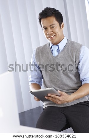 Happy young Asian businessman smiling, using tablet pc, looking at camera.