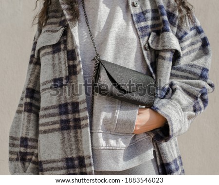 Woman wearing plaid trendy jacket on a gray hoodie with a black leather bag with her hand in her pocket. Royalty-Free Stock Photo #1883546023