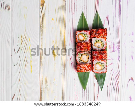 Japanese sushi roll with tempura shrimp served on bamboo leaves on colorful light wooden background. Cucumber and black tiger shrimp wrapped in rice with rainbow flying fish roe Tobiko. Masago caviar