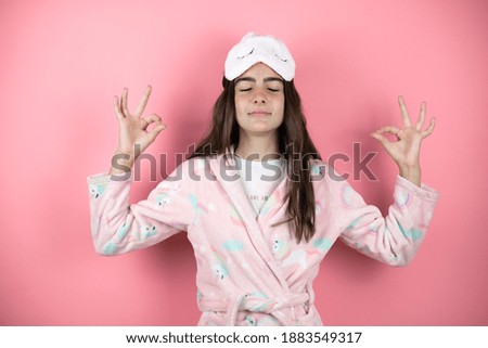Pretty girl wearing pajamas and sleep mask over pink background relax and smiling with eyes closed doing meditation gesture with fingers
