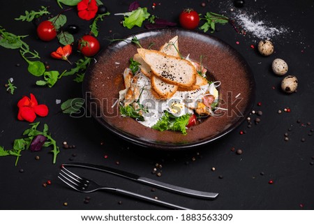 Caesar salad with grilled chicken fillet and slices of bacon, with tomatoes and Caesar sauce. Sprinkled with Parmesan cheese with wheat croutons and quail egg. on a dark background