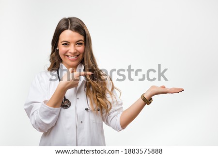 Portrait of smiling medicine student pointing with index finger. Young female doctor with stethoscope on white background