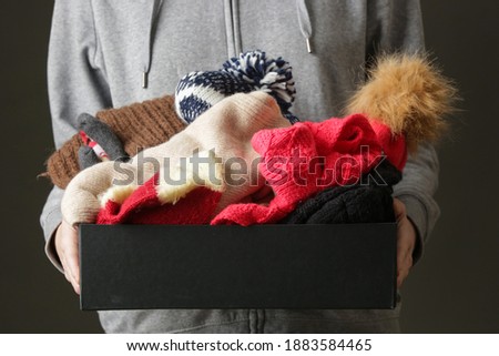 Volunteer women holding donation box with warm woolen wintery clothes, hats, socks, gloves...